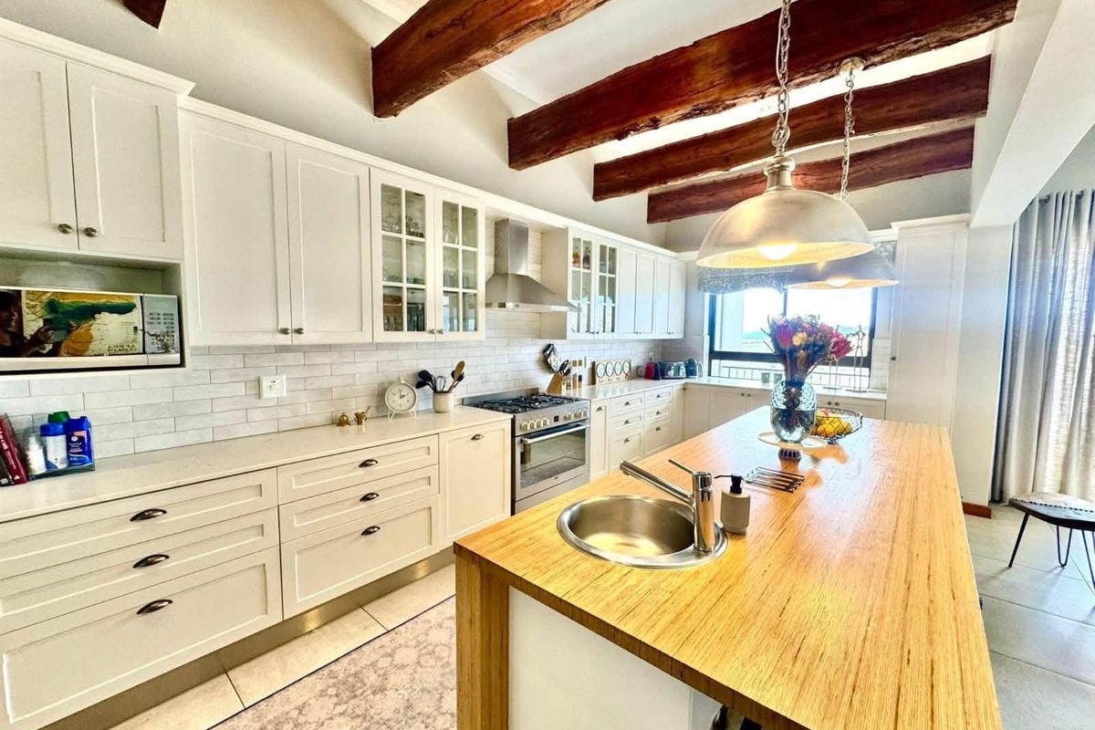 A well-appointed kitchen featuring white shaker cabinetry, subway tile backsplash, a central island with a butcher block countertop, and rustic exposed timber ceiling beams.