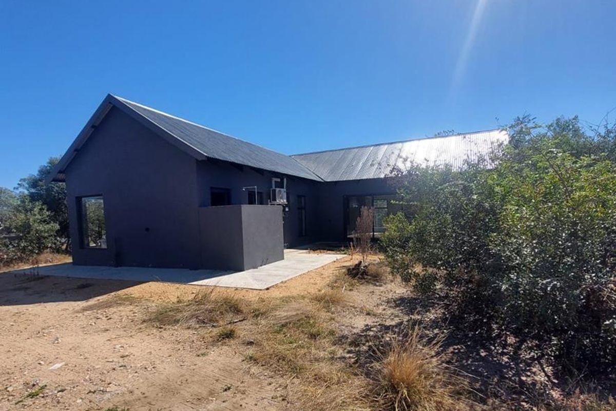 Rear view of a modern dark-painted house featuring a corrugated metal roof, a concrete patio, and an external shower unit.