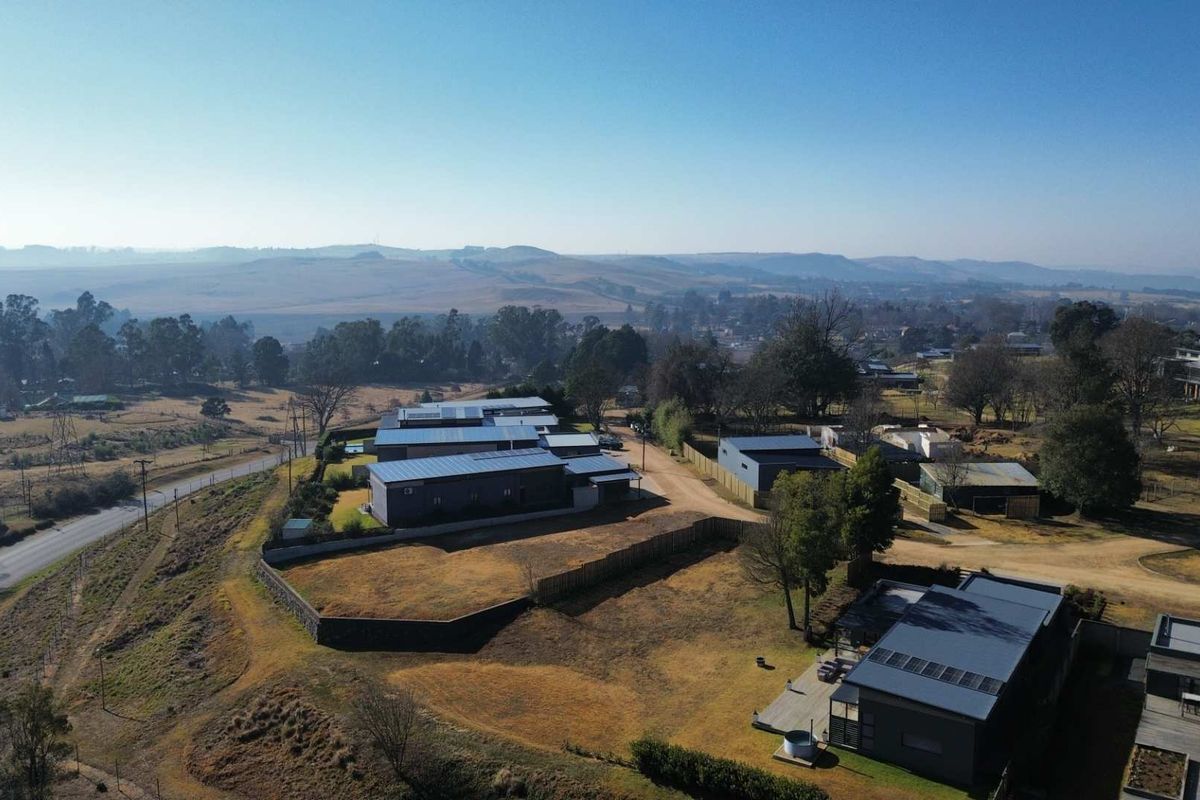 Aerial view of a residential property development featuring modern buildings with metal roofs, surrounding fencing, and expansive landscape views.