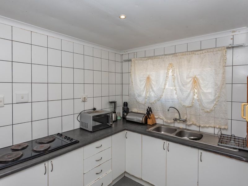 A functional kitchen featuring white cabinetry, dark laminate countertops, a double stainless steel sink, and an electric hob with tiled splashbacks.