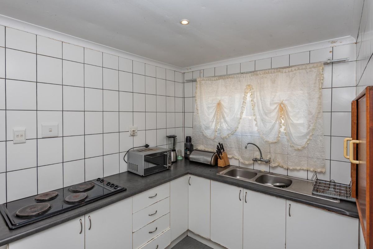 A functional kitchen featuring white cabinetry, dark laminate countertops, a double stainless steel sink, and an electric hob with tiled splashbacks.