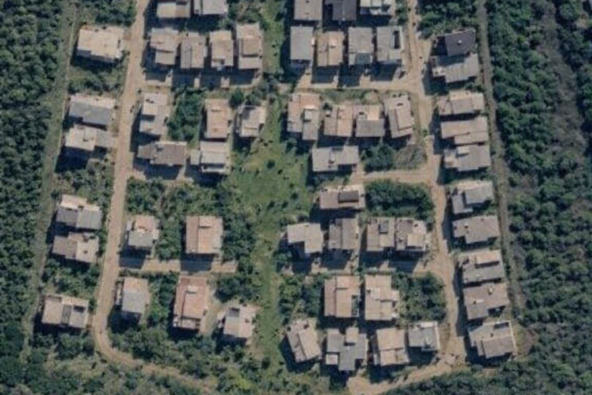 An aerial view of a residential estate development showing the layout of individual plots, internal roads, and surrounding natural vegetation.
