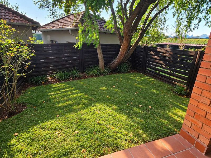 A private rear garden featuring a well-maintained lawn, timber slat fencing, and a brick-pillared patio area.