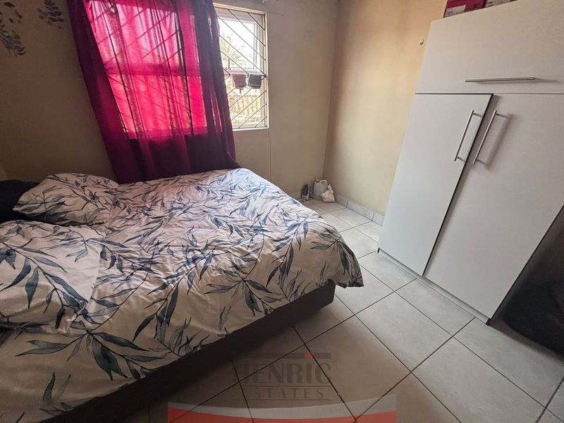 A bedroom featuring tiled flooring, a built-in wardrobe, and a window fitted with security burglar bars.