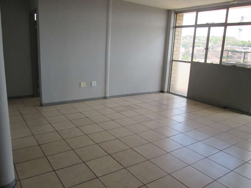 An empty, open-plan living area featuring ceramic floor tiles and large windows with natural light, offering a blank canvas for renovation.
