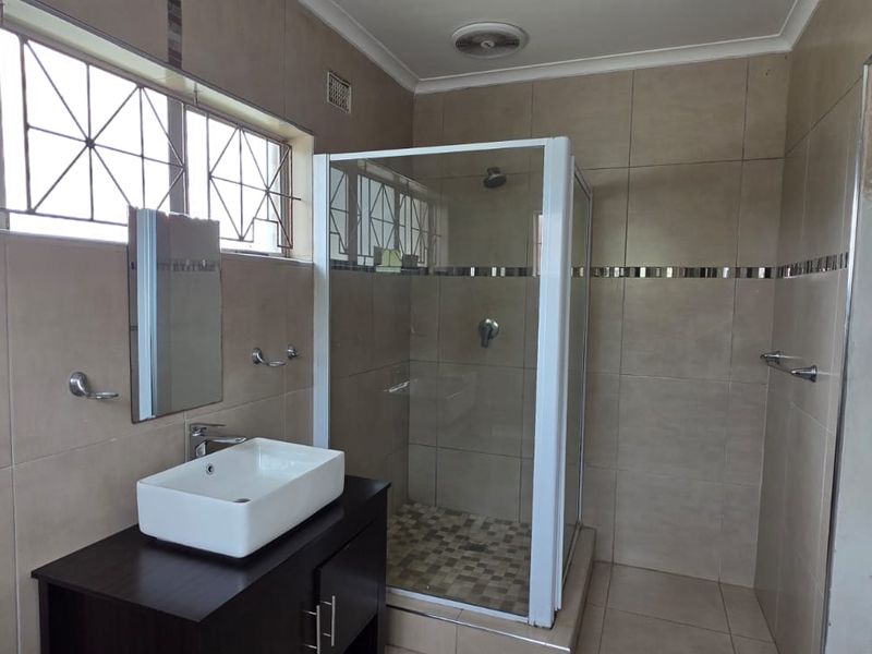 A functional bathroom featuring a glass-enclosed shower, a modern vessel sink on a vanity cabinet, and neutral wall tiling throughout.