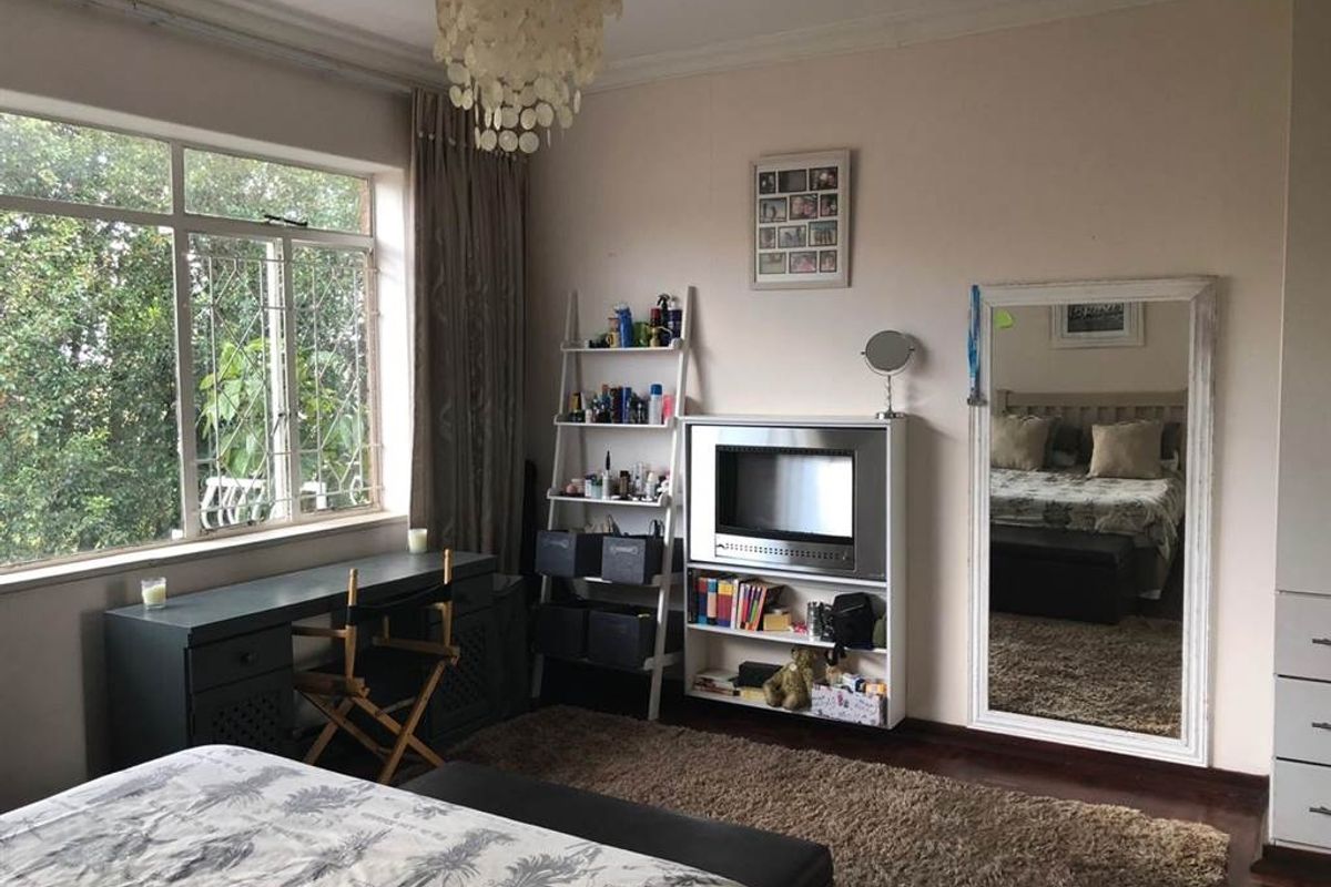 A spacious bedroom featuring large windows with security bars, dark wood flooring, and built-in storage cabinetry.