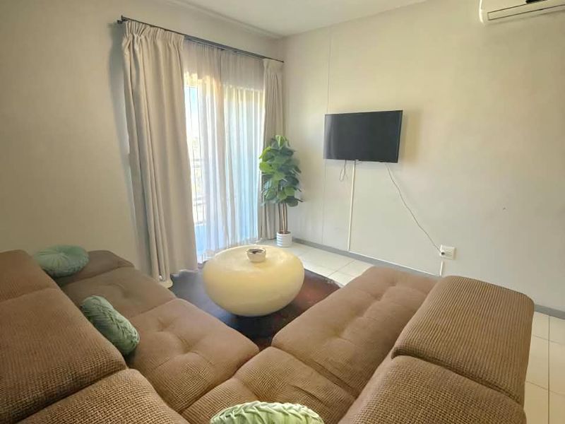A comfortable living room featuring tiled flooring, a wall-mounted air conditioning unit, and a sliding glass door providing access to the exterior.