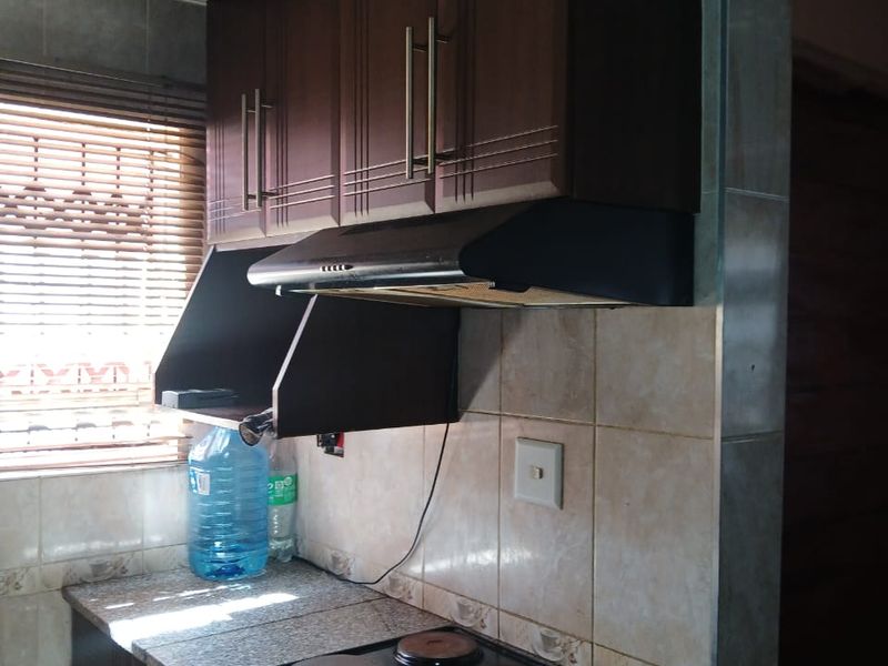 A functional kitchen area featuring dark wood cabinetry, a built-in electric hob with extractor fan, granite countertops, and tiled wall finishes.