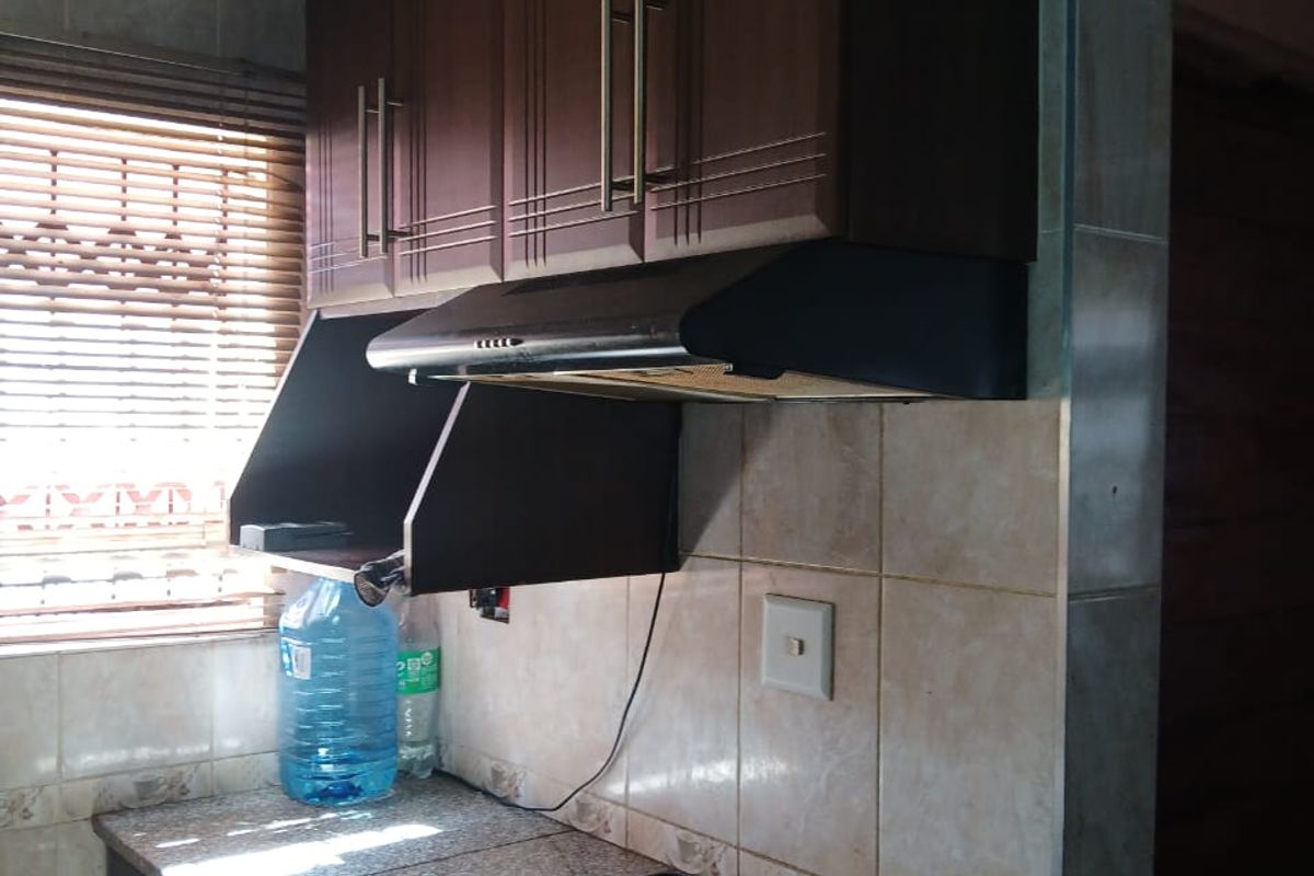 A functional kitchen area featuring dark wood cabinetry, a built-in electric hob with extractor fan, granite countertops, and tiled wall finishes.