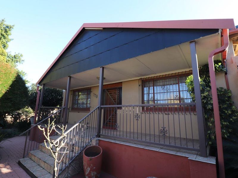 Front elevation of the house featuring a covered porch, tiled entrance stairs, and metal security bars on the windows.