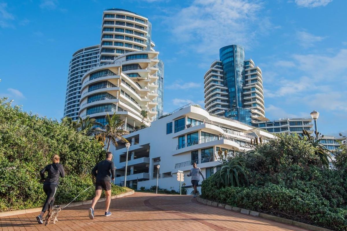 A scenic view of modern high-rise apartment buildings set against a clear blue sky, featuring paved walkways and landscaped surroundings.