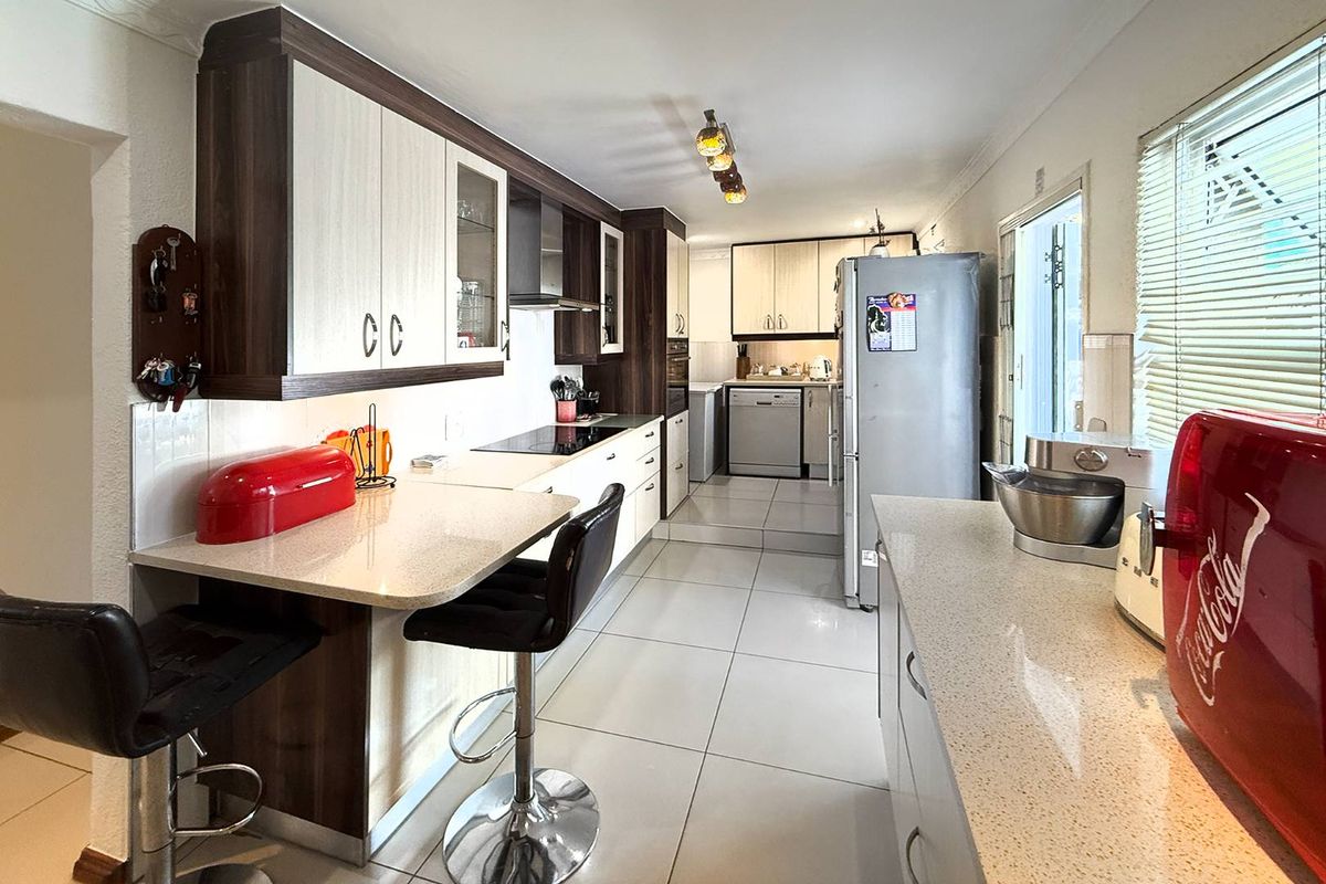 A functional kitchen featuring built-in cabinetry, stone-look countertops, a breakfast nook, and tiled flooring, leading into a secondary scullery area.