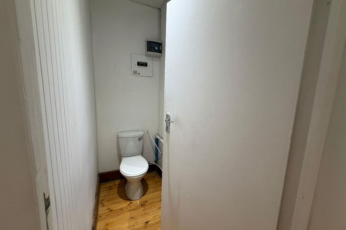 A small, functional office restroom featuring a standard toilet, timber flooring, and wall-mounted electrical distribution board.