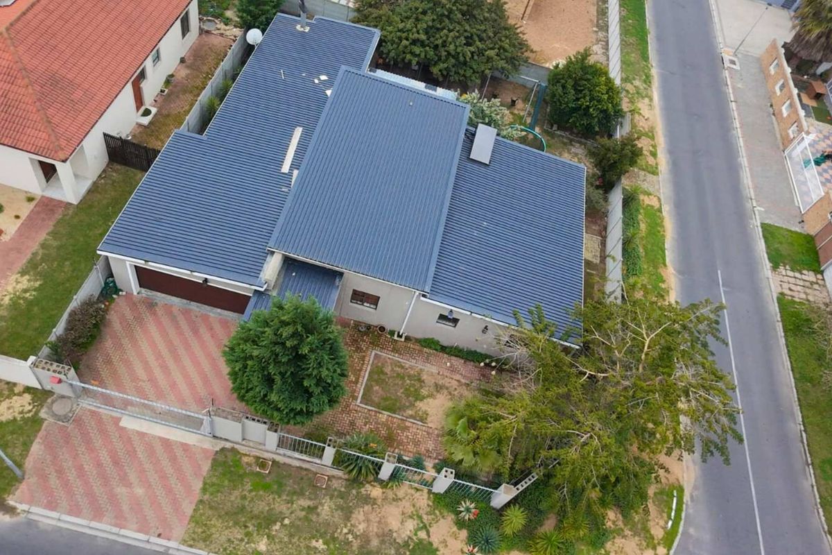 Aerial view of a residential property featuring a metal roof, paved driveway, attached garage, and established garden area.