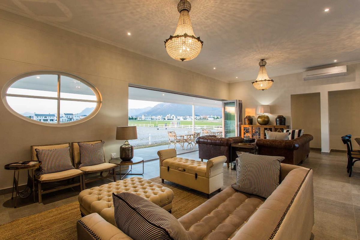Spacious living area featuring large sliding doors opening to an outdoor patio, elegant crystal chandeliers, and a unique oval window with scenic views.