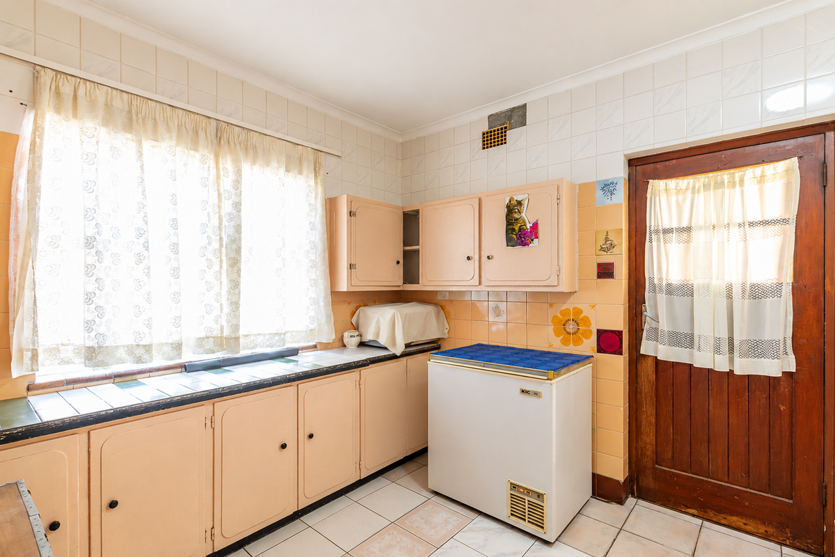 A dated kitchen featuring original cabinetry, tiled backsplash, and tiled flooring, offering significant potential for a modern renovation.