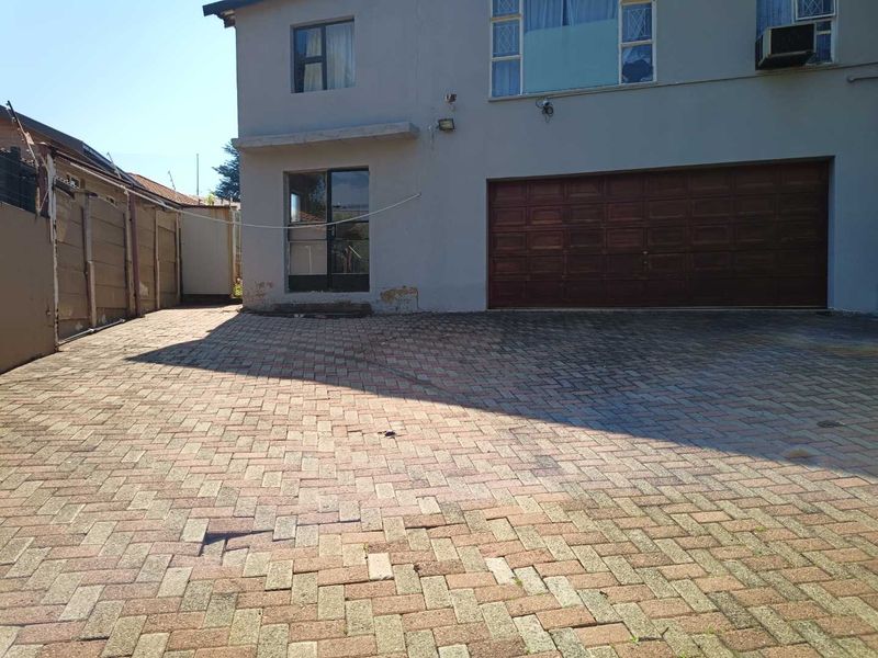 Front exterior view of a two-story house featuring a paved driveway, double garage, and sliding door access, showing signs of wear and maintenance needs.