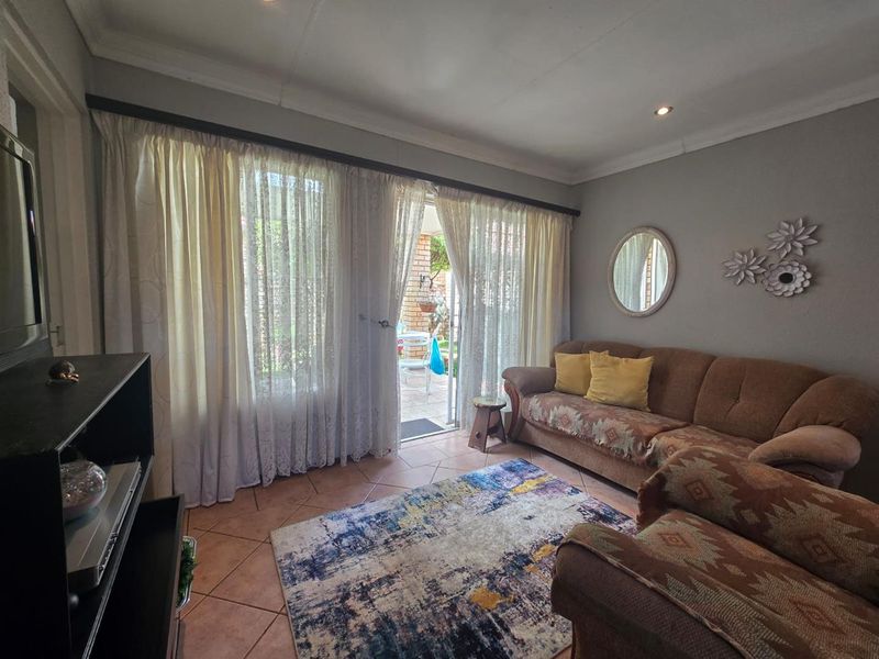 A cozy living room featuring tiled flooring, coved ceilings, and a sliding glass door providing direct access to the outdoor patio area.