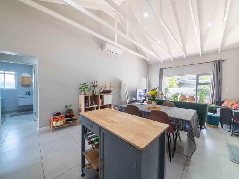 Spacious open-plan living and dining area featuring high vaulted ceilings with exposed rafters, tiled flooring, and direct access to the outdoor patio.
