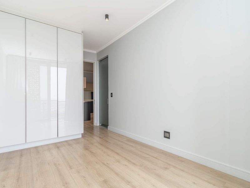 A bright, modern bedroom featuring high-gloss built-in wardrobes, light laminate flooring, and clean finishes, offering a versatile space ready for personalization.