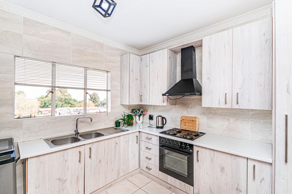 Modern kitchen featuring light wood-grain cabinetry, stone-look wall tiles, a built-in oven with hob, extractor fan, and a double stainless steel sink.