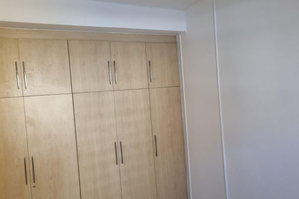 A bedroom featuring light wood-finish built-in cupboards with modern metal handles, providing ample storage space.