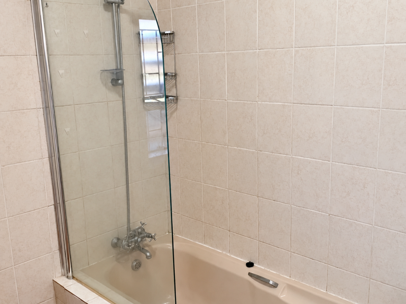 A functional bathroom featuring a bathtub with a glass shower screen, wall-mounted shower mixer, and tiled surround.