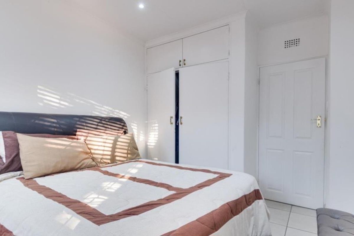 A bright bedroom featuring built-in cupboards, tiled flooring, and recessed downlighting, offering a clean and functional living space.