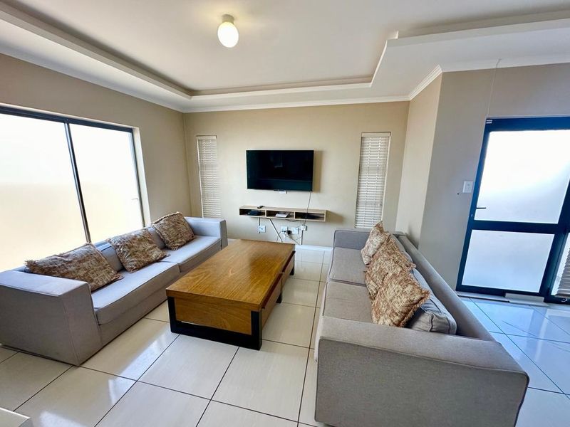 A bright, modern living room featuring tiled floors, a recessed ceiling, and a floating media console with direct access to outdoor space.