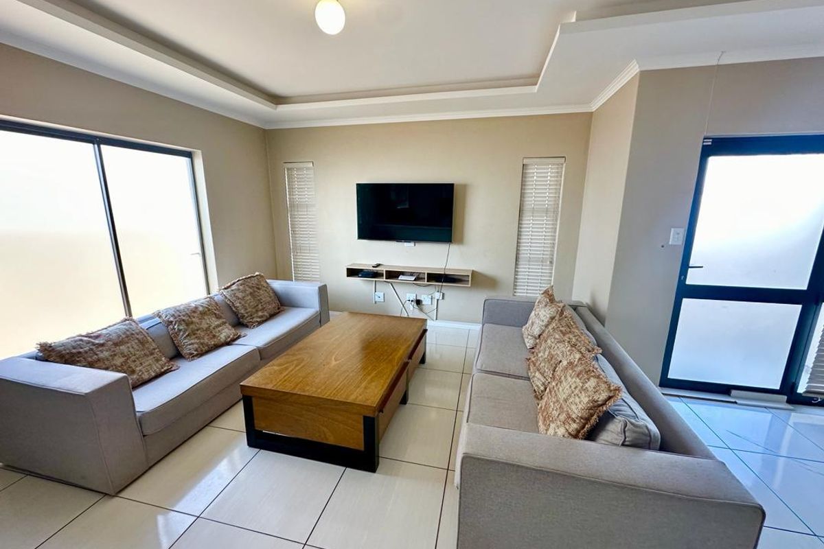 A bright, modern living room featuring tiled floors, a recessed ceiling, and a floating media console with direct access to outdoor space.