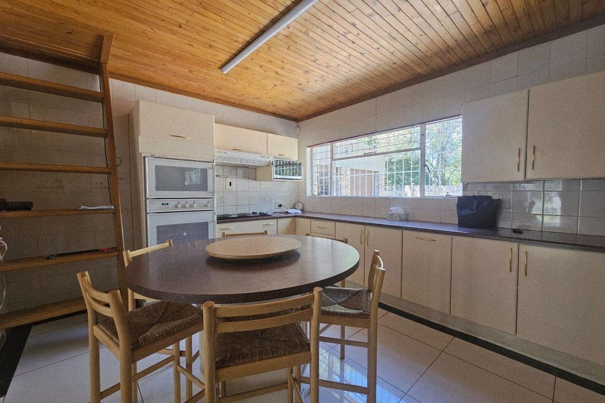 A functional kitchen featuring built-in cabinetry, integrated oven and hob, tiled flooring, and a distinctive timber-clad ceiling.