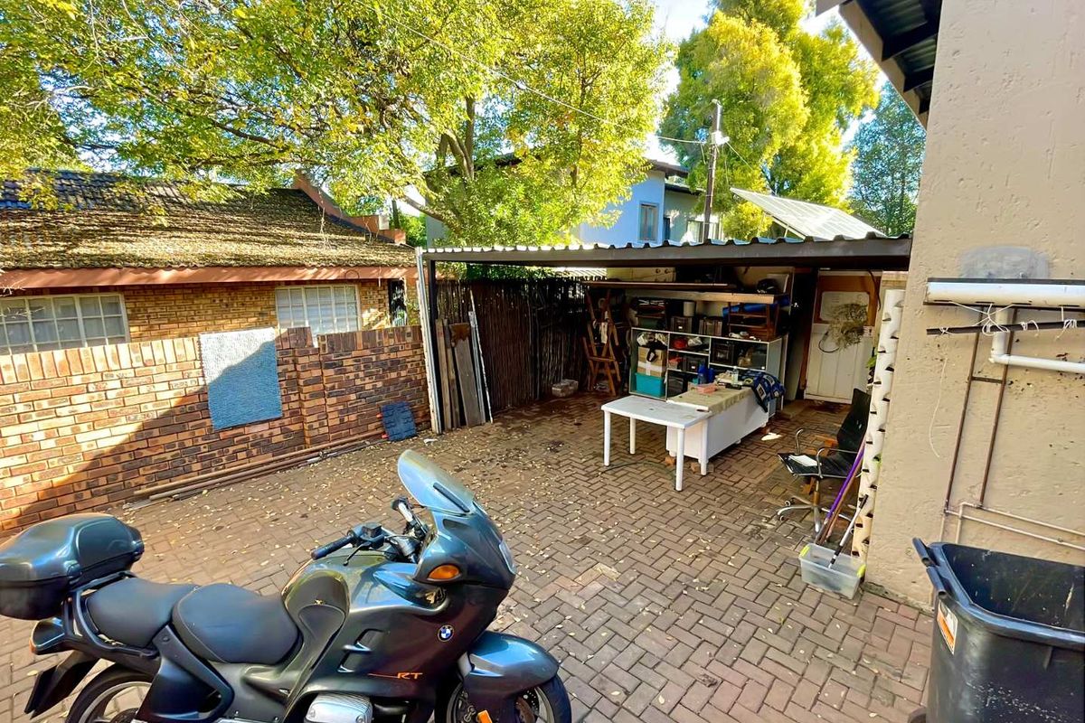 A rear outdoor area featuring brick paving, a brick boundary wall, and a covered carport structure.