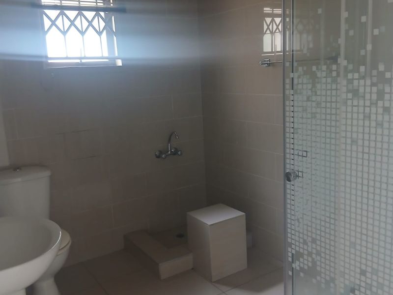 A clean, neutral-toned bathroom featuring a pedestal basin, toilet, and a glass-enclosed shower with tiled finishes throughout.
