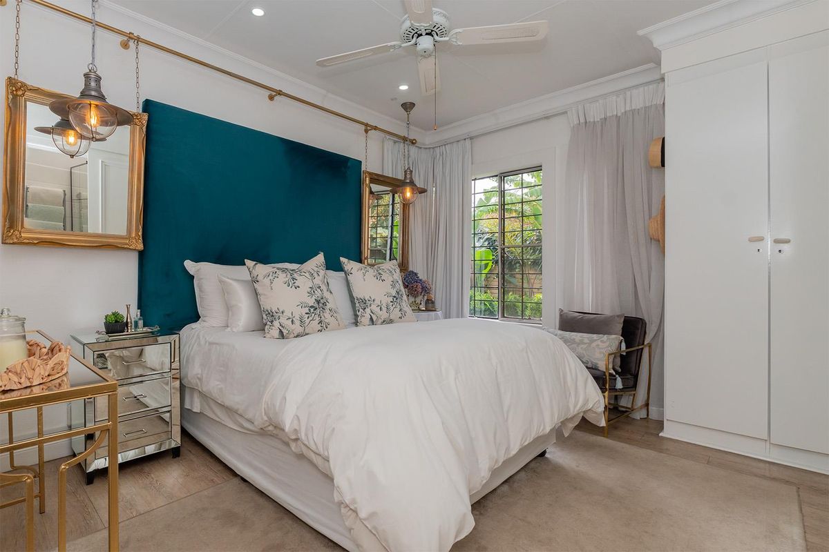 A well-appointed bedroom featuring built-in floor-to-ceiling cabinetry, a ceiling fan, and large windows overlooking the garden.