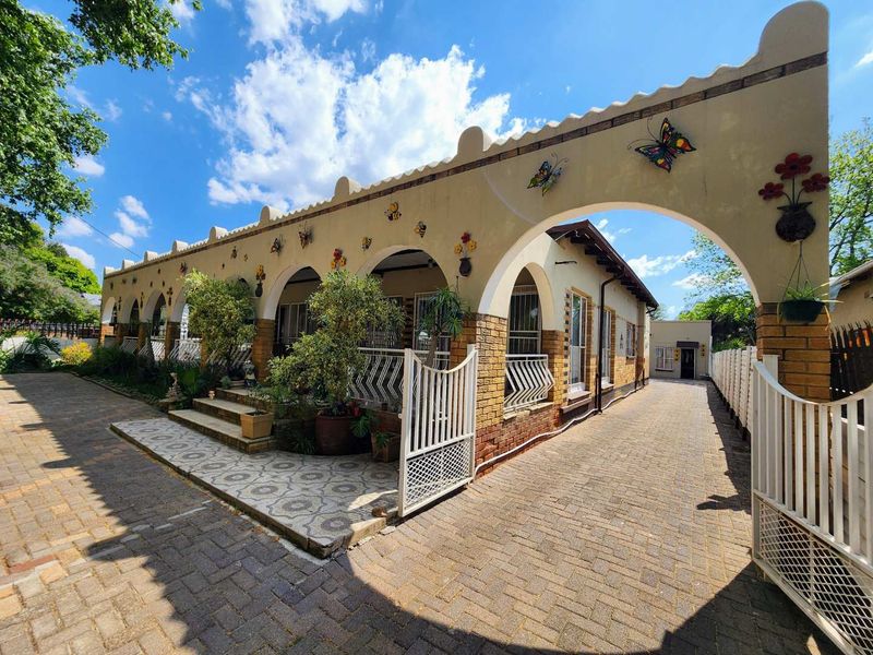 A charming front exterior featuring a distinctive arched facade, brick-paved driveway, and a tiled patio area with secure gated access.