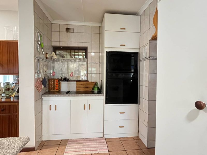 A compact kitchen area featuring built-in cabinetry, a wall-mounted oven, tiled backsplash, and tiled flooring, offering a functional but dated layout.