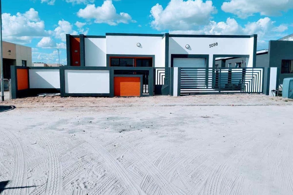 Modern single-story residential facade featuring a contemporary color scheme, secure boundary wall, sliding gate, and integrated garage access.
