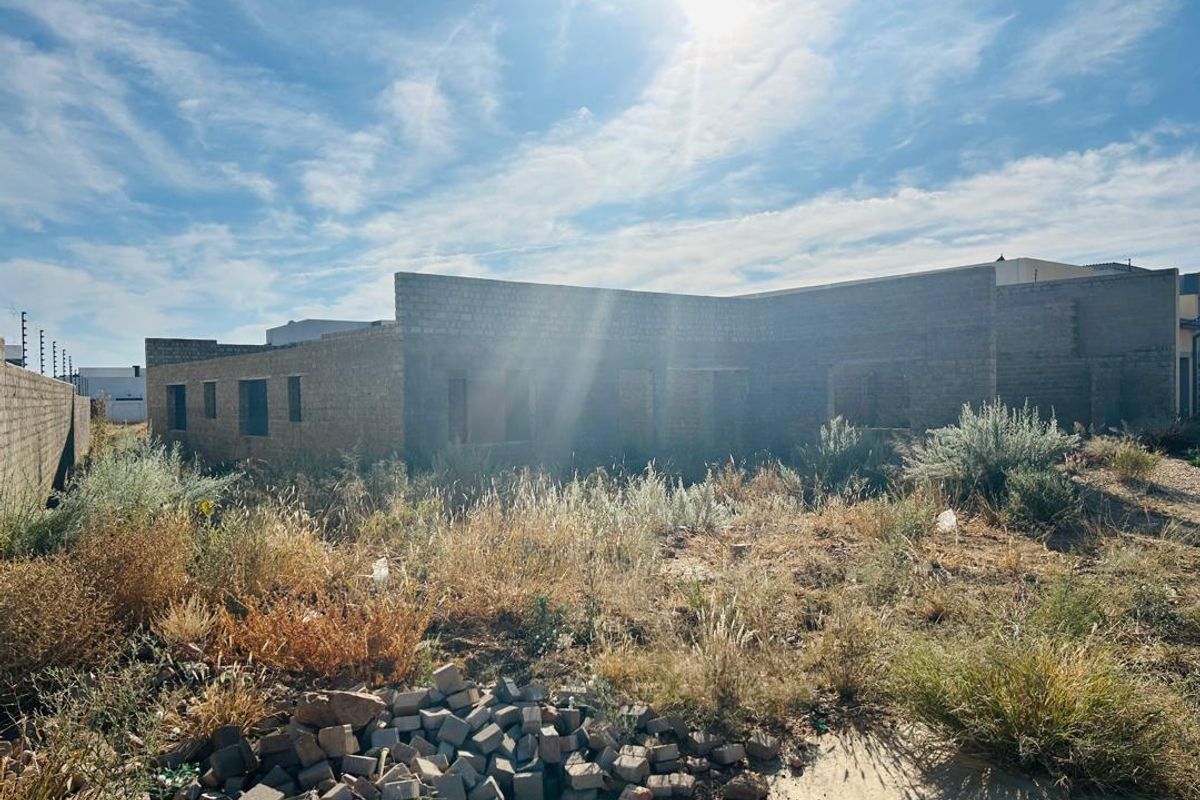 A view of a residential property currently under construction, featuring exposed masonry walls and an overgrown site requiring significant development.