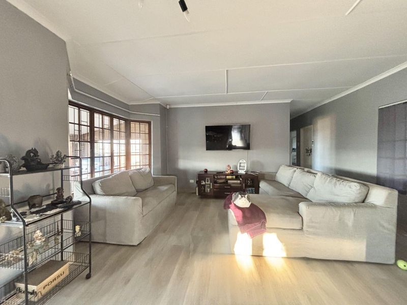 Spacious living room featuring light-toned laminate flooring, a large bay window, and neutral wall finishes, providing a comfortable and bright family area.