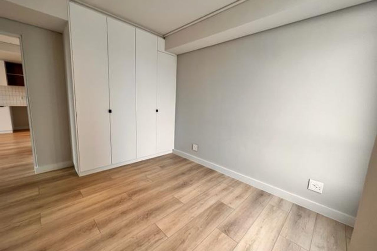 A bright, empty bedroom featuring modern laminate flooring and floor-to-ceiling built-in cupboards, offering a clean and neutral space ready for furnishing.