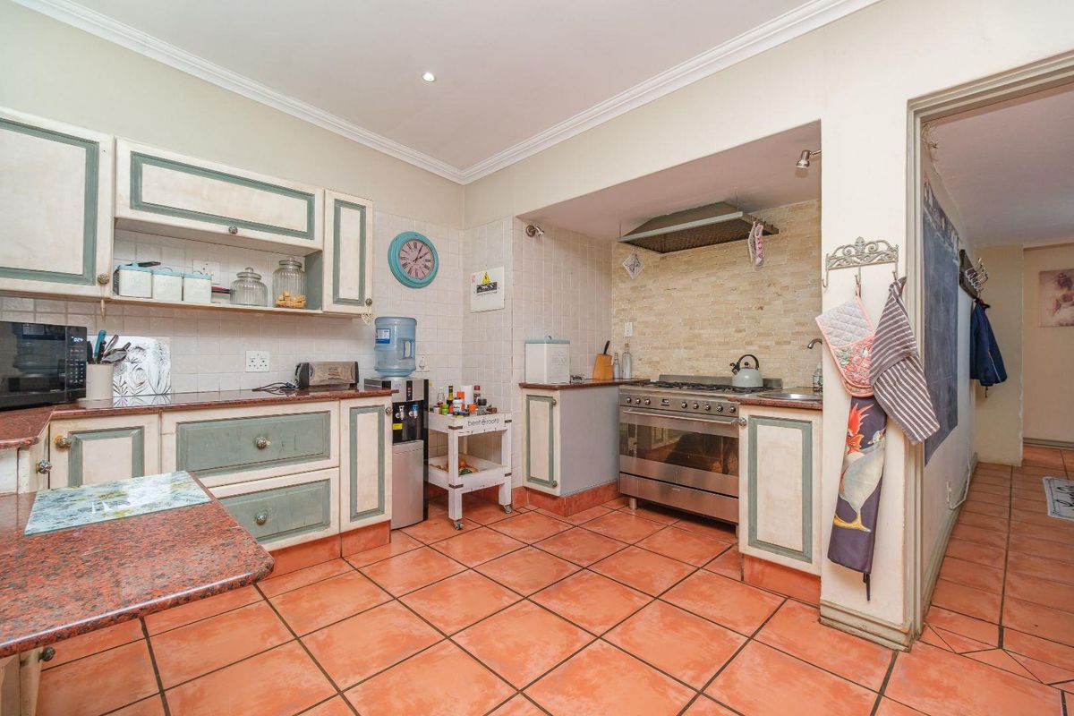A functional kitchen featuring built-in cabinetry, granite countertops, a gas stove with extractor fan, and terracotta-style tiled flooring.