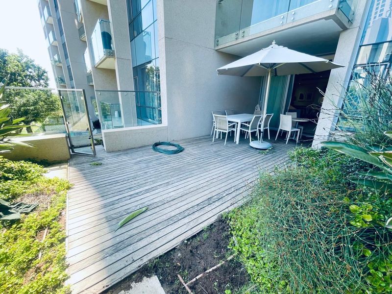 A ground-floor apartment patio featuring timber decking, glass balustrades, and direct access to the interior living space.