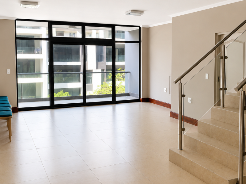 Spacious open-plan living area featuring neutral tiled flooring, a modern staircase with glass balustrades, and large sliding doors leading to a balcony.