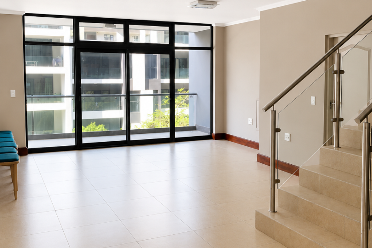 Spacious open-plan living area featuring neutral tiled flooring, a modern staircase with glass balustrades, and large sliding doors leading to a balcony.