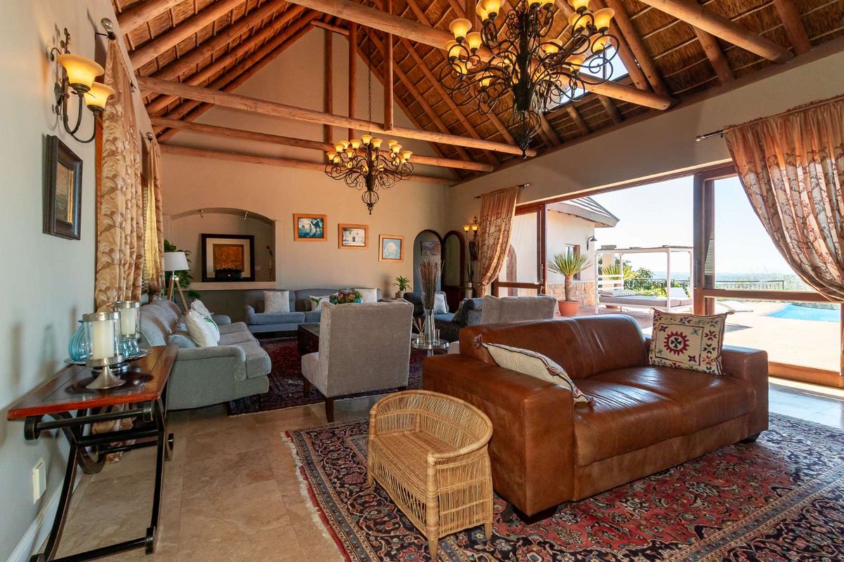 Spacious living room featuring a high vaulted thatched ceiling with exposed timber rafters, stone flooring, and large sliding doors opening to the patio.