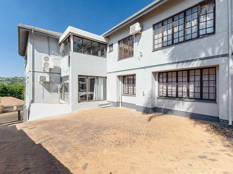 Rear exterior view of the property featuring a paved courtyard, multi-level facade with steel-framed windows, and wall-mounted air conditioning units.
