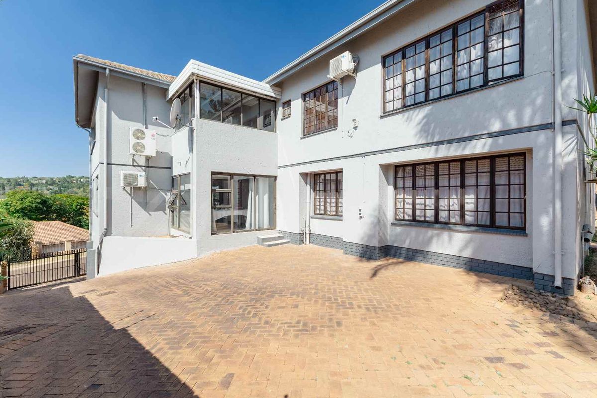 Rear exterior view of the property featuring a paved courtyard, multi-level facade with steel-framed windows, and wall-mounted air conditioning units.