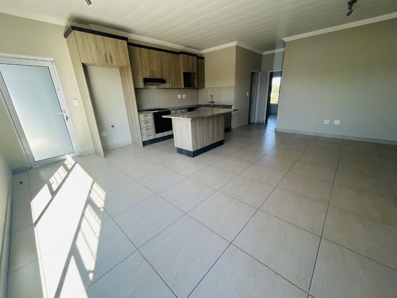 Spacious open-plan living and kitchen area featuring modern wood-look cabinetry, a central island, and neutral tiled flooring throughout.