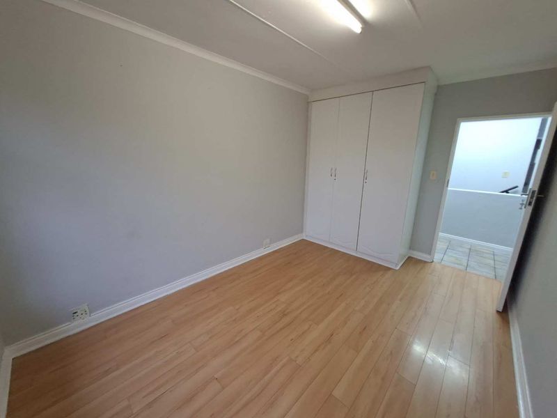 A clean, empty bedroom featuring light-toned laminate flooring and a built-in white wardrobe, offering a neutral canvas for personalization.